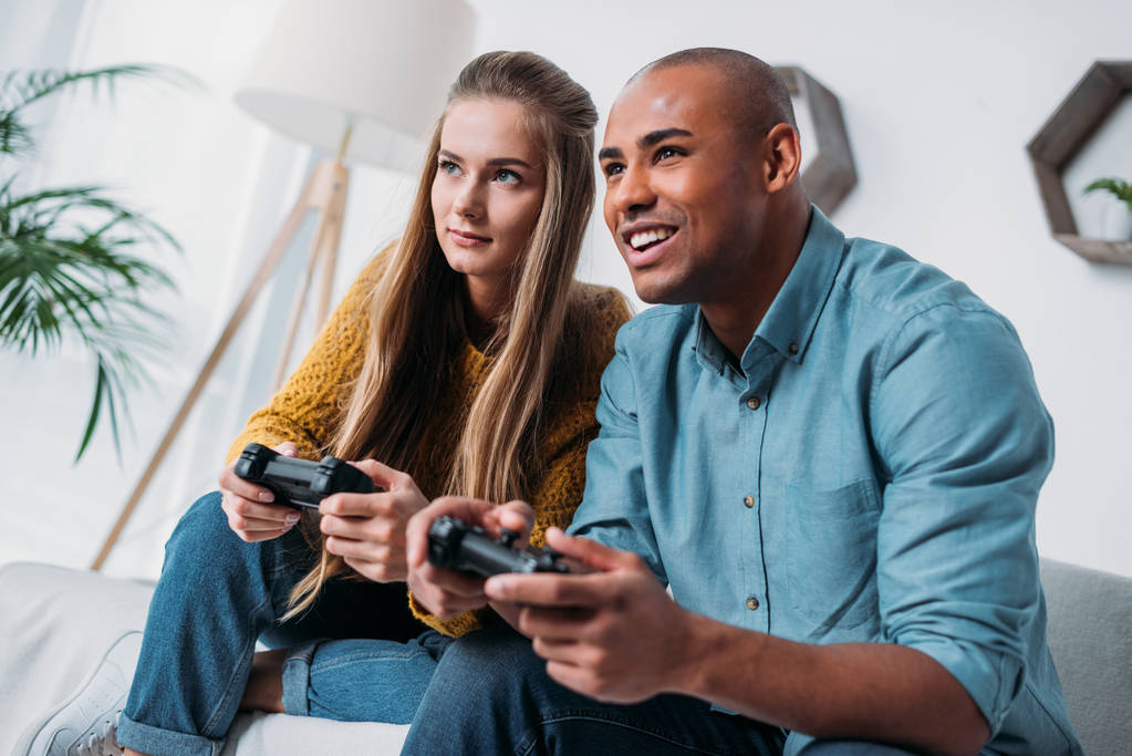 sonriente pareja multicultural jugando videojuego en casa
 - Foto, Imagen