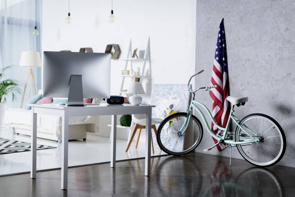 ordenador de plata en la mesa y la bicicleta cerca de la pared en la habitación
 - Foto, Imagen