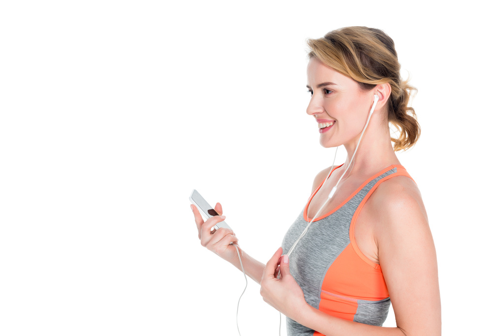 femme souriante en vêtements de sport écouter de la musique dans les écouteurs isolés sur blanc
 - Photo, image