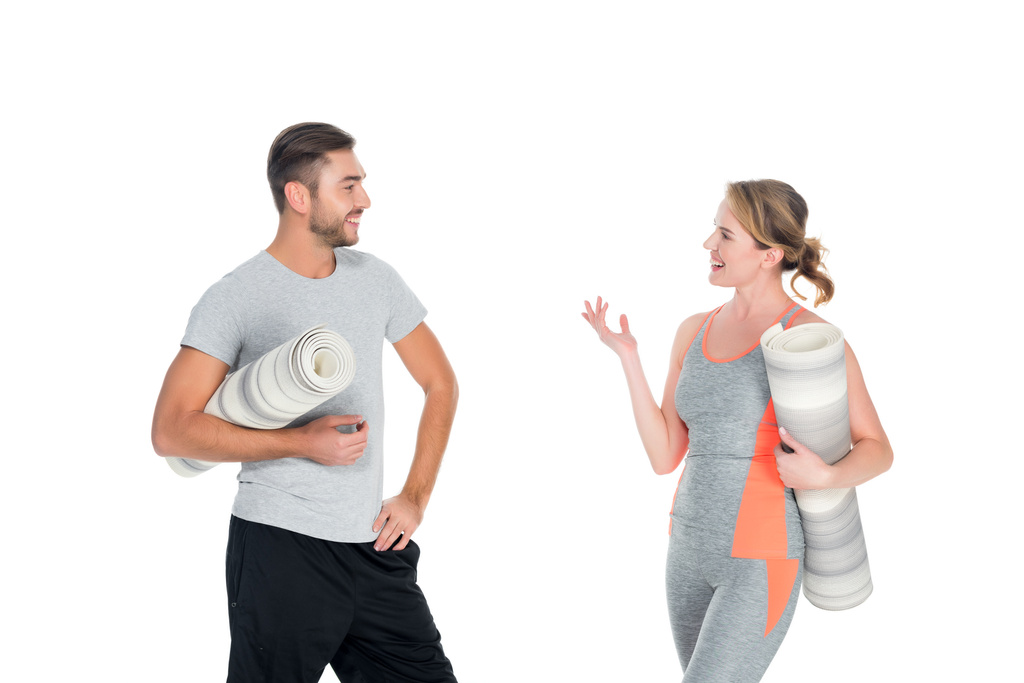 Porträt eines sportlichen Paares mit Yogamatten, die sich isoliert auf weißen Matten unterhalten - Foto, Bild