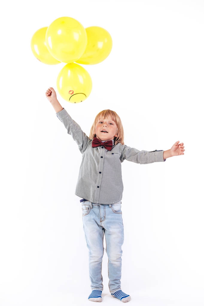 Κομψό μικρό αγόρι ντυμένος με κόκκινο παπιγιόν κρατώντας αερόστατο που απομονώνονται σε λευκό φόντο. Χαμόγελο. - Φωτογραφία, εικόνα
