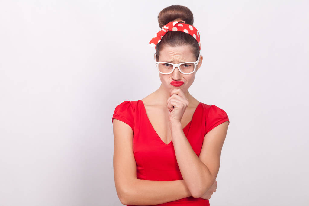 nachdenkliche Frau in rotem Kleid und mit Brille vor grauem Hintergrund, Brainstorming-Konzept - Foto, Bild