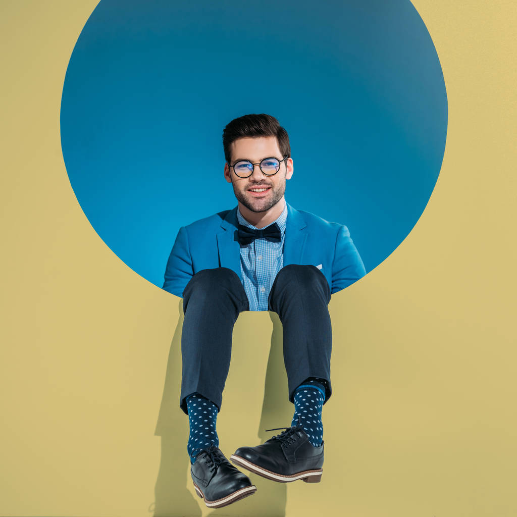 hymyilevä komea mies muodikkaissa vaatteissa istuu pyöreä beige aukko
 - Valokuva, kuva