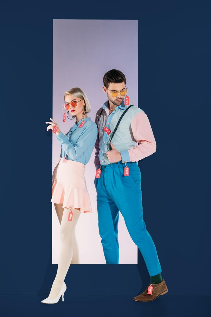 attraktives Paar in modischer Kleidung mit Verkaufsetiketten isoliert auf blau - Foto, Bild