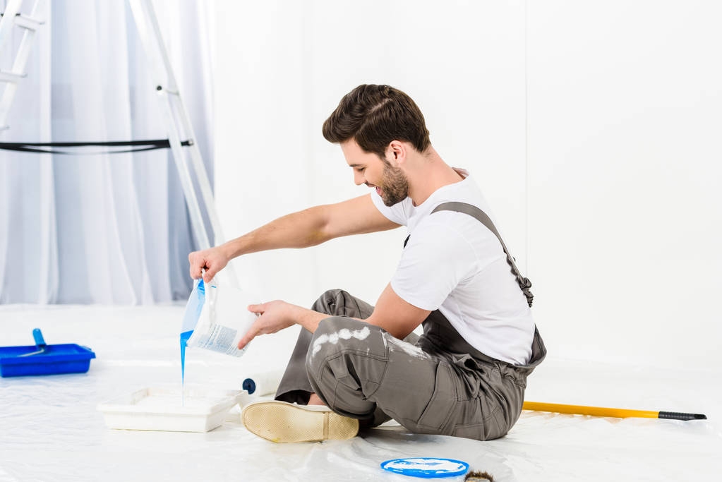 side view of handsome man pouring paint into tray - Photo, Image