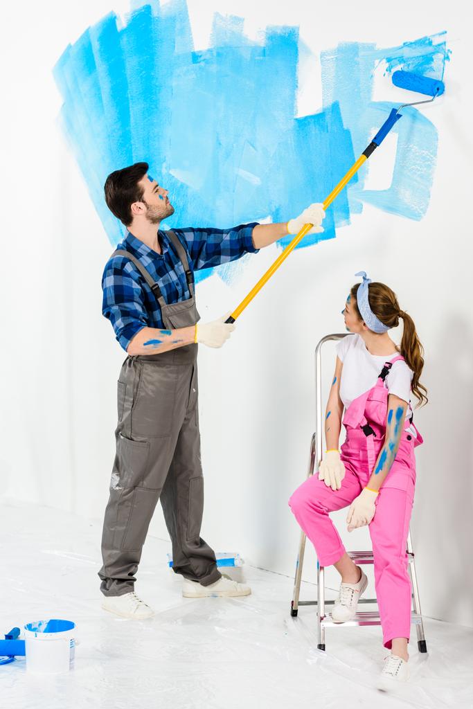 vriendje schilderen muur en vriendin zittend op de ladder - Foto, afbeelding