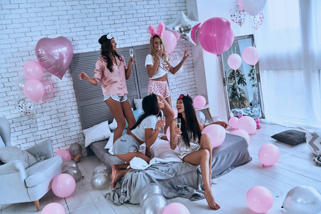 schöne junge lächelnde Frauen im Pyjama feiern Junggesellenabschied mit Champagner im Schlafzimmer mit Luftballons - Foto, Bild