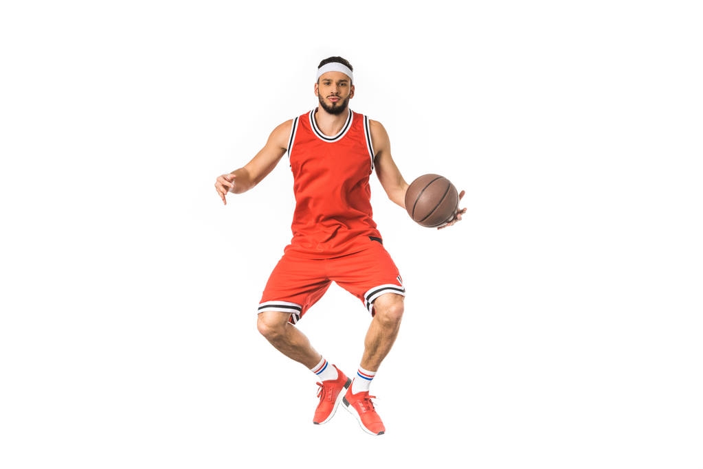 knappe jonge basketbalspeler springen met bal en kijken naar camera geïsoleerd op wit  - Foto, afbeelding