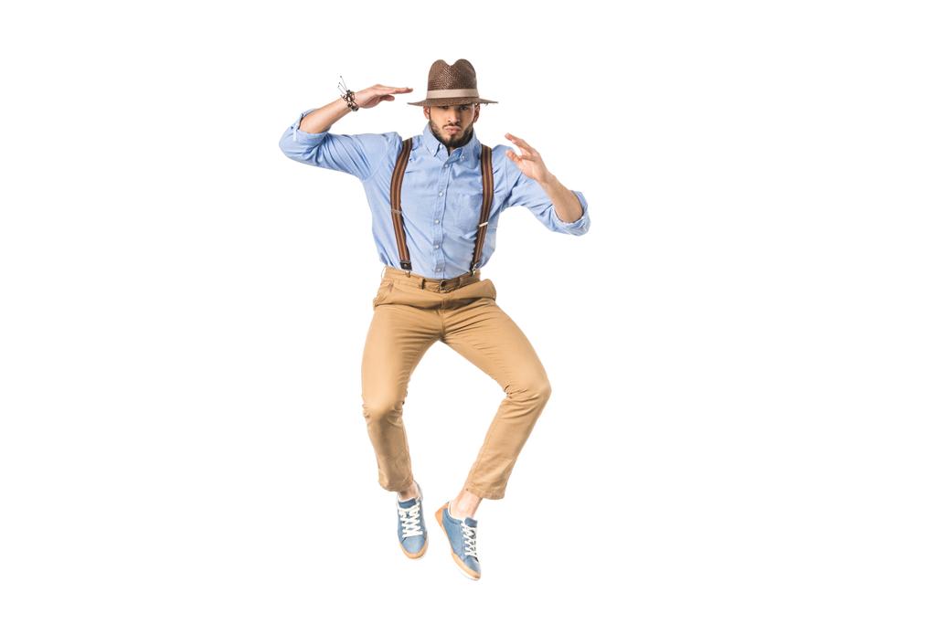 stylischer junger Mann mit Hut springt und blickt vereinzelt in die Kamera - Foto, Bild
