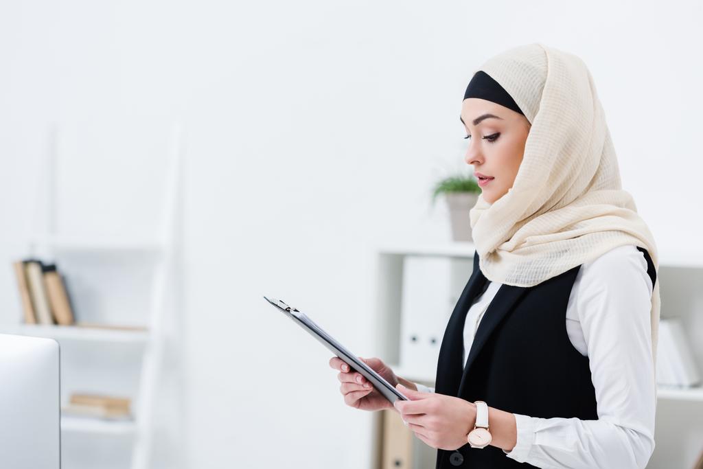 フォルダーとヒジャーブのイスラム教徒女性実業家のサイドビューのオフィスで手します。 - 写真・画像
