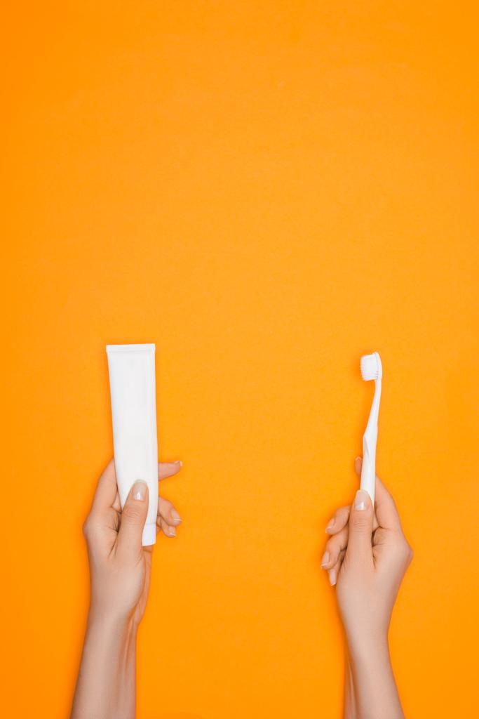 bijgesneden beeld van vrouw met tandenborstel en een tube tandpasta, geïsoleerd op oranje - Foto, afbeelding