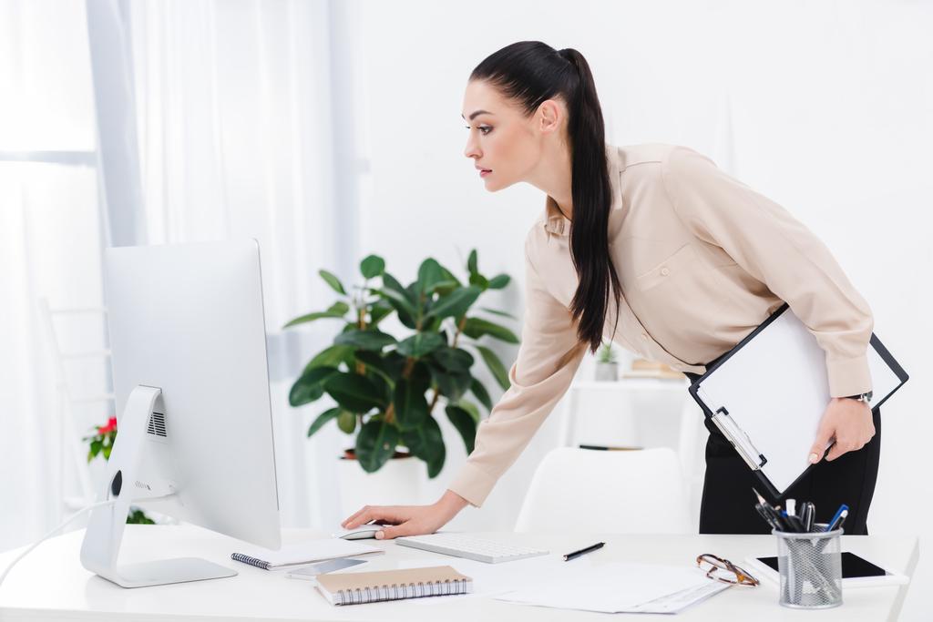 vista lateral de la mujer de negocios con bloc de notas trabajando en la computadora en el lugar de trabajo
 - Foto, Imagen