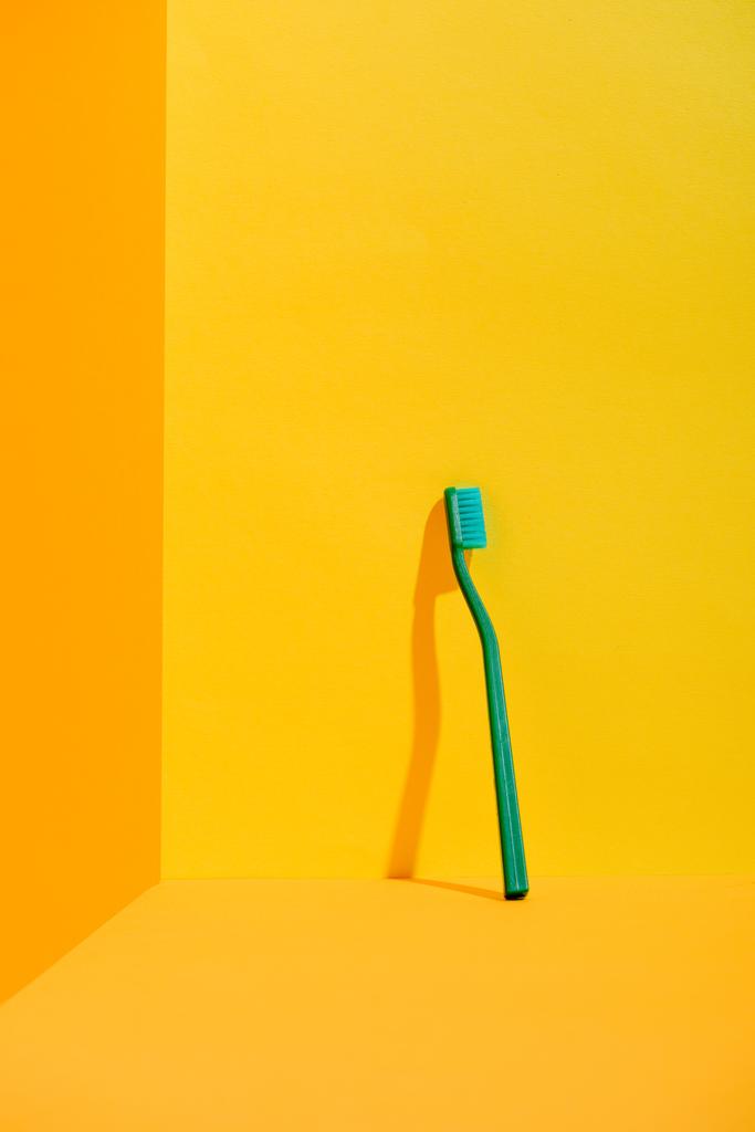 groene tandenborstel staande bij oranje muur - Foto, afbeelding
