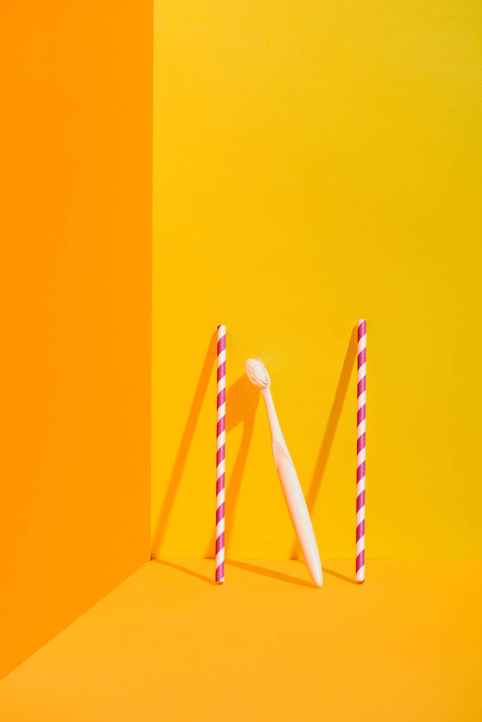 rietjes en witte tandenborstel staande bij oranje muur - Foto, afbeelding