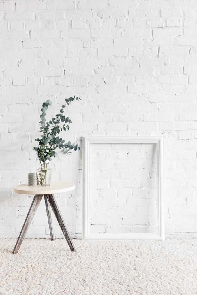 marco vacío frente a la pared de ladrillo blanco con maceta de flores en la mesa, concepto de maqueta
 - Foto, imagen