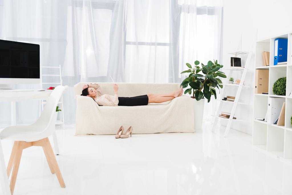 Seitenansicht einer Geschäftsfrau mit digitalem Tablet im Büro auf Sofa liegend - Foto, Bild