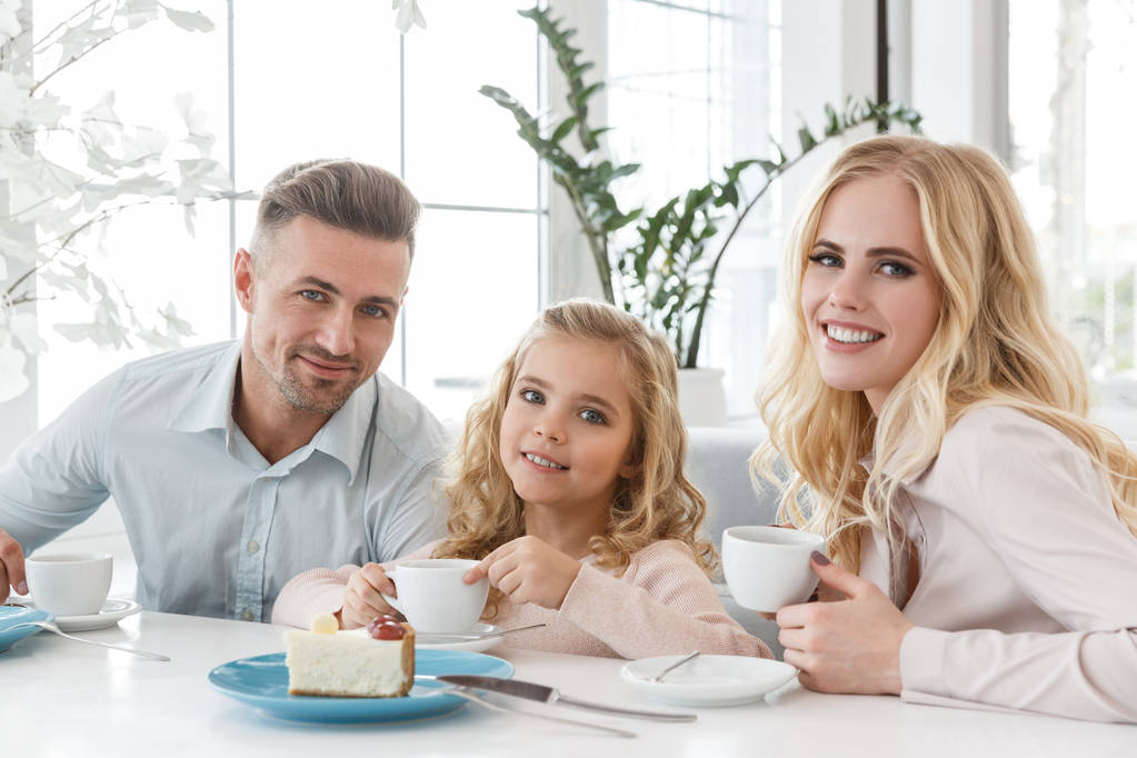 jovem família com xícaras de café e bolo passar tempo no café
 - Foto, Imagem