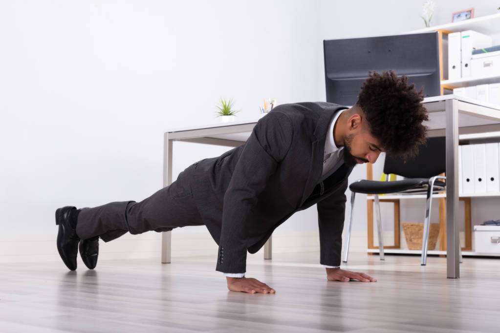 Nuori liikemies tekee push up lattialla työpaikalla
 - Valokuva, kuva