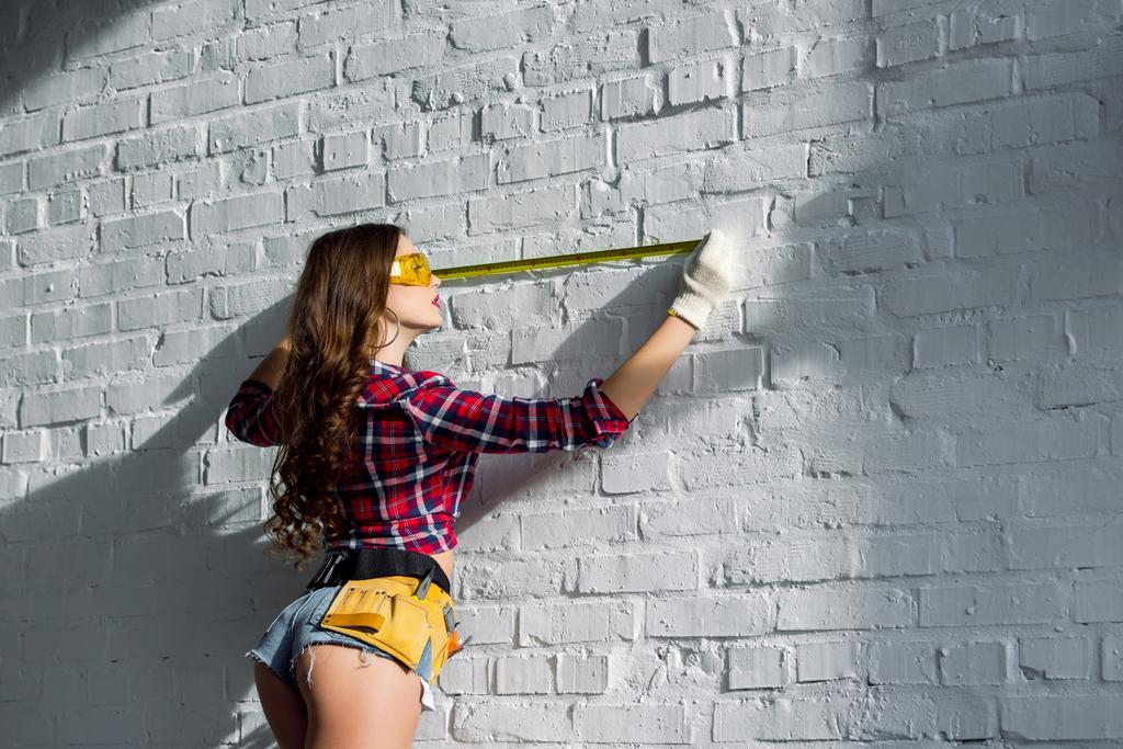 seksi kadın beyaz kemer Kesici takımlar için ölçme ile tuğla duvar - Fotoğraf, Görsel