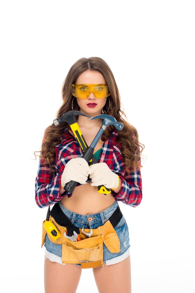 mooi meisje in bril en handschoenen met gereedschap riem holding hamers, geïsoleerd op wit - Foto, afbeelding