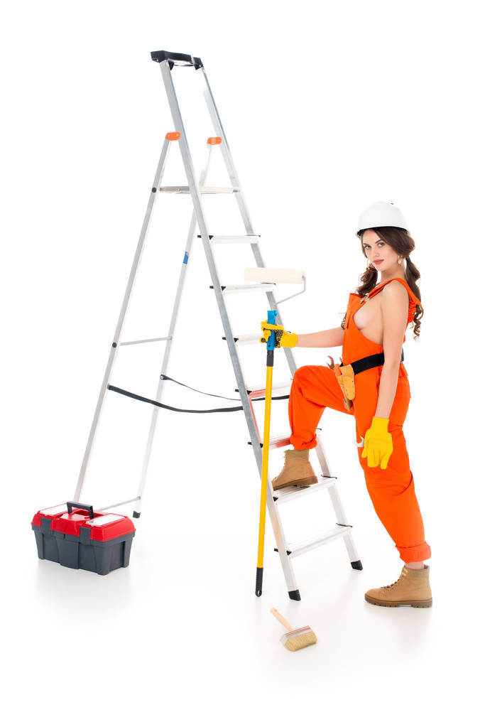 hermosa trabajadora sosteniendo rodillo de pintura cerca de escalera y caja de herramientas, aislado en blanco
 - Foto, imagen