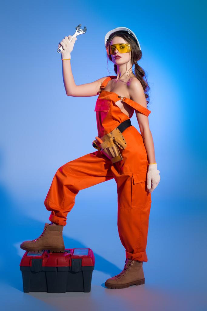 hermosa chica en overoles con cinturón de herramientas y caja de herramientas que sostiene la llave, en azul
 - Foto, imagen