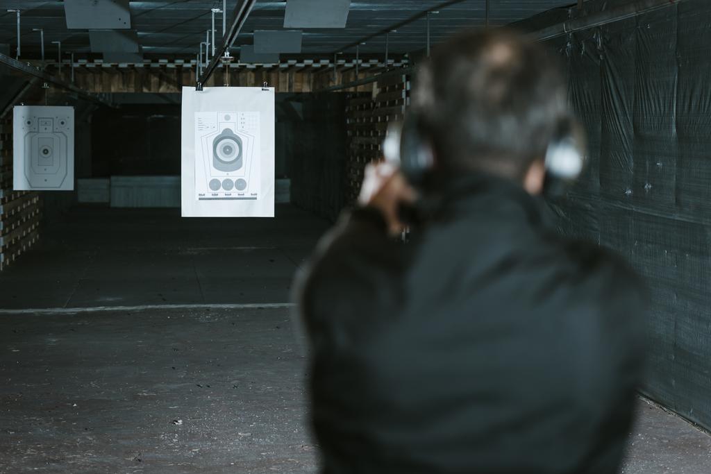 visión trasera del hombre apuntando arma al objetivo en el campo de tiro
 - Foto, imagen