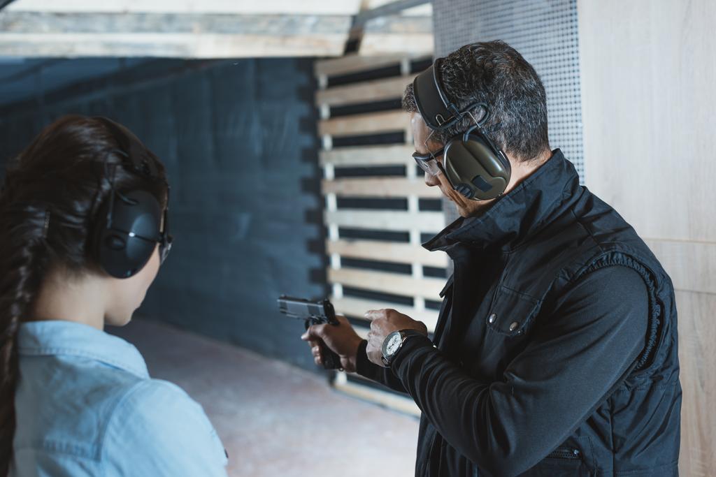 Инструктор-мужчина, описывающий пистолет клиентке в тире
 - Фото, изображение