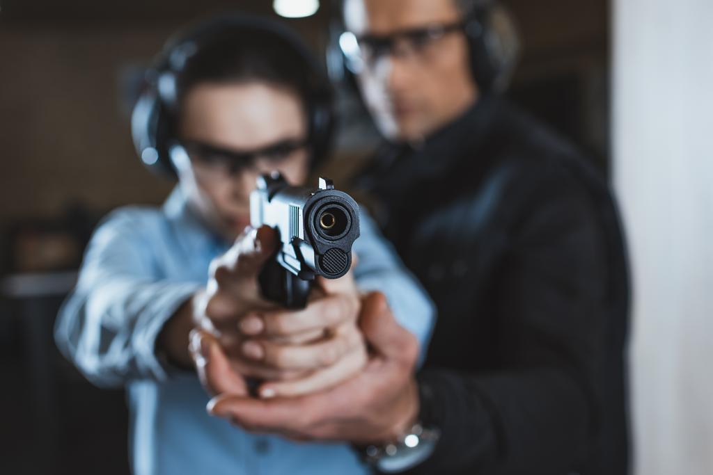 Ausbilder hilft Kundin im Schießstand mit Waffe im Vordergrund - Foto, Bild
