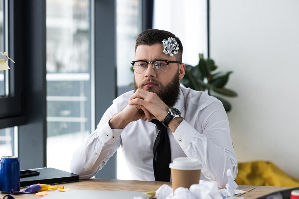 Porträt eines nachdenklichen Geschäftsmannes mit Schleife am Kopf am Arbeitsplatz im Büro - Foto, Bild