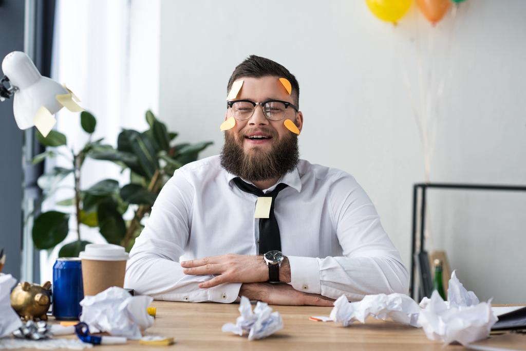 Porträt eines gut gelaunten Geschäftsmannes in formeller Kleidung mit klebrigen Zetteln im Gesicht am Arbeitsplatz im Büro - Foto, Bild