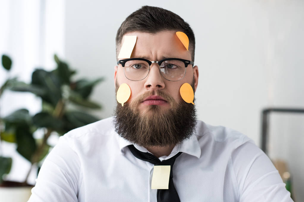 portrait of serious businessman in formal wear with sticky notes on face - Photo, Image