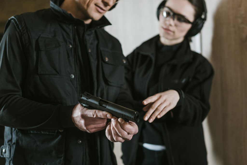 Ausgeschnittenes Bild eines Ausbilders, der einer Kundin in Schießbude Waffe zeigt - Foto, Bild