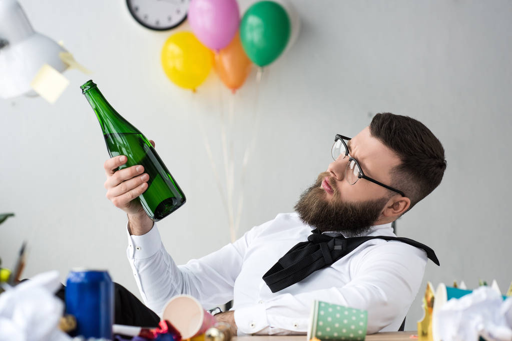 zakenman met fles champagne zit op werkplek op kantoor - Foto, afbeelding