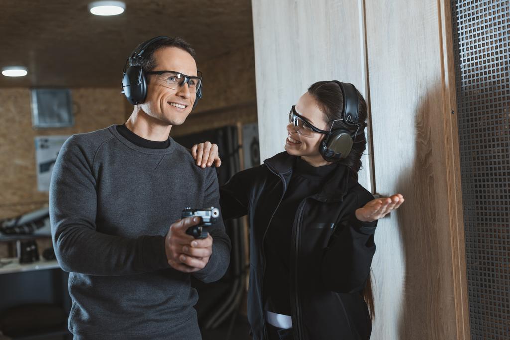 smiling shooting instructor supporting client in shooting gallery - Photo, Image