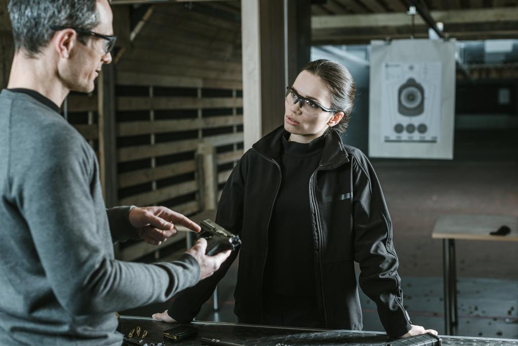 ohjaaja kuvailee asetta naisasiakkaalle ampumaradalla
 - Valokuva, kuva