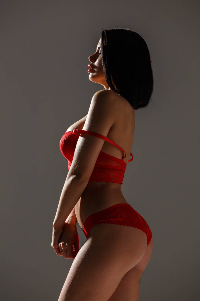 Studio βολή της όμορφη μελαχρινή γυναίκα που φοράει κόκκινα εσώρουχα. Νεαρά ομορφιά γυναίκα να στέκεται στην πλευρά φως στο φόντο γκρι στούντιο  - Φωτογραφία, εικόνα