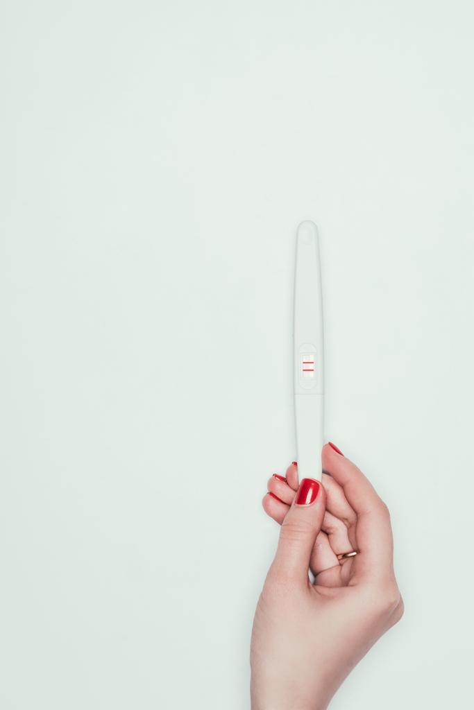 Μερική άποψη της γυναίκας κρατώντας τεστ εγκυμοσύνης με δύο γραμμές στο χέρι απομονωθεί σε λευκό  - Φωτογραφία, εικόνα