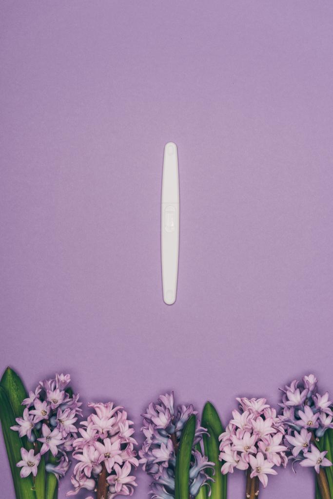 Draufsicht auf arrangierte Blumen und Schwangerschaftstest isoliert auf lila  - Foto, Bild