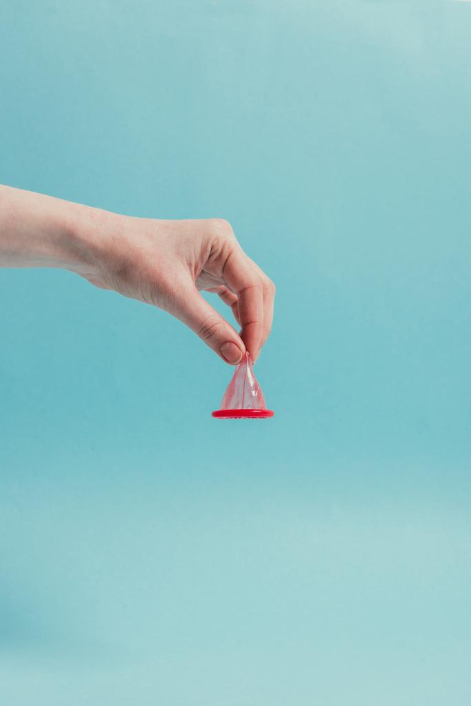 Teilansicht der Frau mit geöffnetem Kondom in der Hand isoliert auf blauem Grund - Foto, Bild
