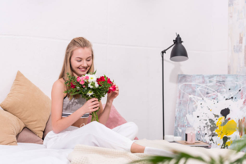 attractive young woman with beautiful bouquet sitting on bed at home - Photo, Image