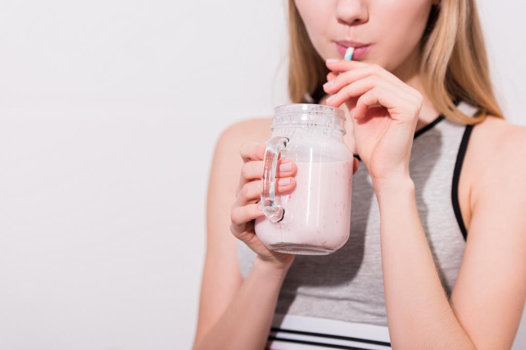 bijgesneden schot van jonge vrouw milkshake drinken uit mason jar met rietje - Foto, afbeelding
