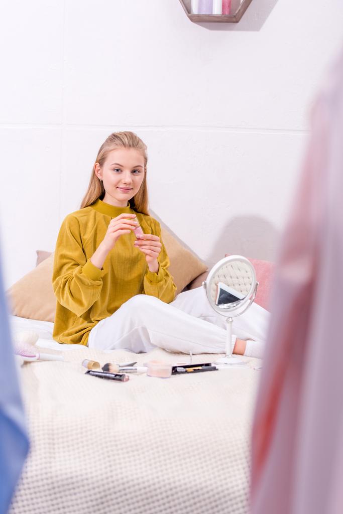 jeune femme faisant du maquillage tout en étant assis sur le lit à la maison
 - Photo, image