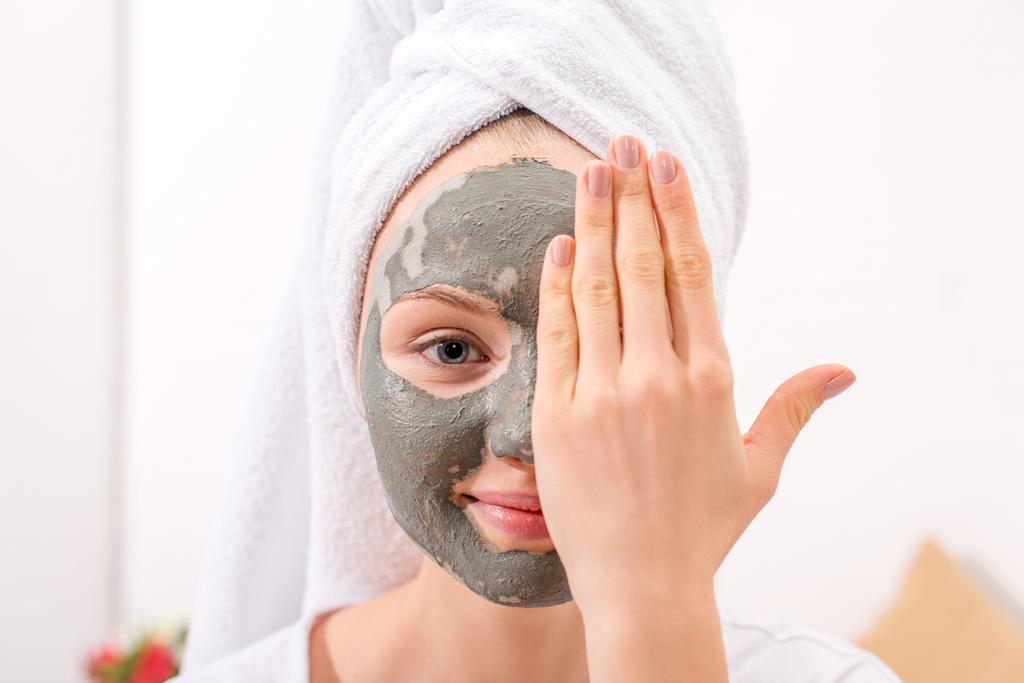 mladá žena s kosmetickým jílová maska pokrývá polovinu obličeje - Fotografie, Obrázek
