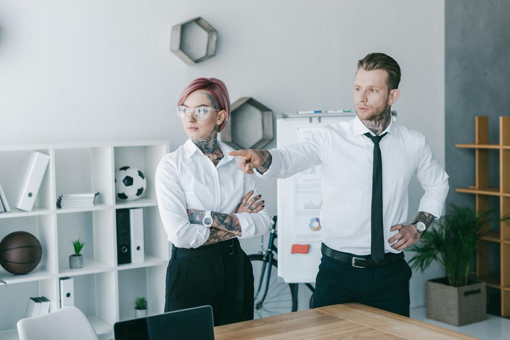 νέοι επιχειρηματίες με τατουάζ ψάχνει μακριά ενώ στέκεται μαζί στο γραφείο - Φωτογραφία, εικόνα