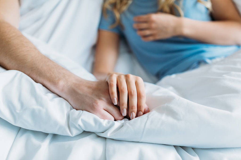 обрізане зображення пари, що тримає руки в ліжку
 - Фото, зображення