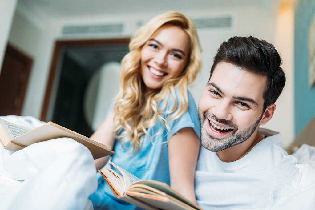 smiling couple with books in bed looking at camera - Photo, Image