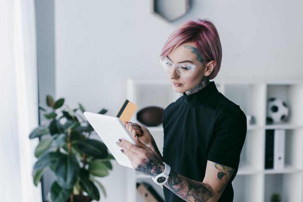 молодая татуированная предпринимательница в очках, держащая кредитную карту и пользующаяся
 - Фото, изображение