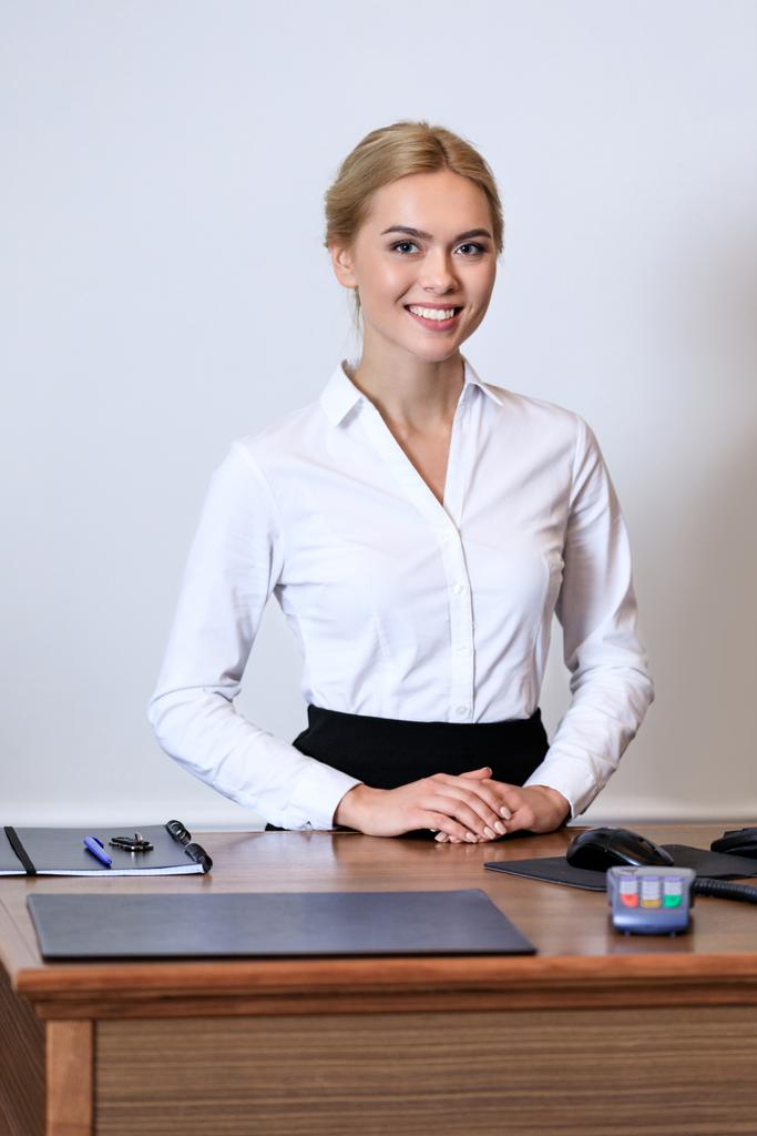 smiling attractive receptionist standing at reception desk in hotel - Photo, Image