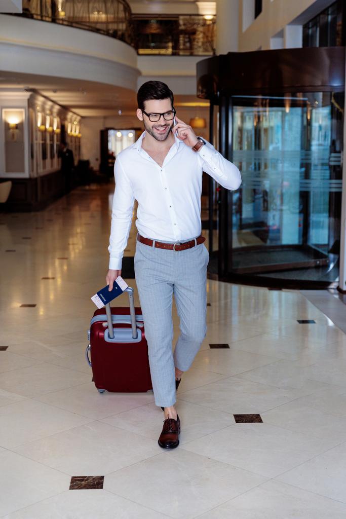 handsome traveler walking in hotel and talking by smartphone  - Photo, Image